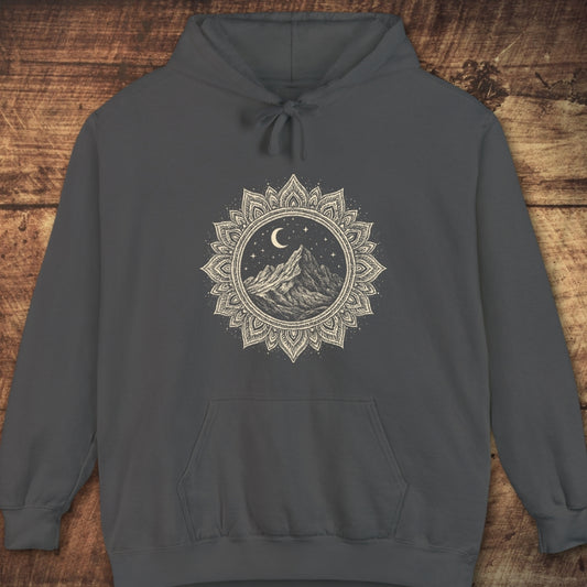 Mountain Mandala Hoodie featuring a hand-drawn mountain graphic under stars and a crescent moon, surrounded by a mandala border. Includes a kangaroo pocket and drawstrings, laid flat on wood.