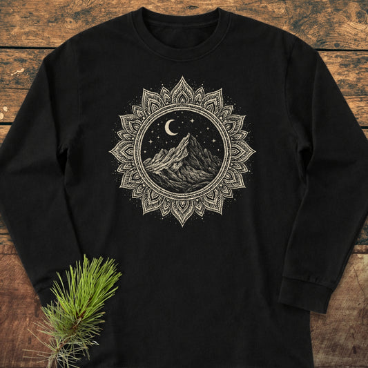 Mountain Mandala Long-Sleeve Tee with a circular mandala graphic featuring a mountain scene, stars, and crescent moon on soft, 100% ring-spun cotton, laid on a wooden surface.