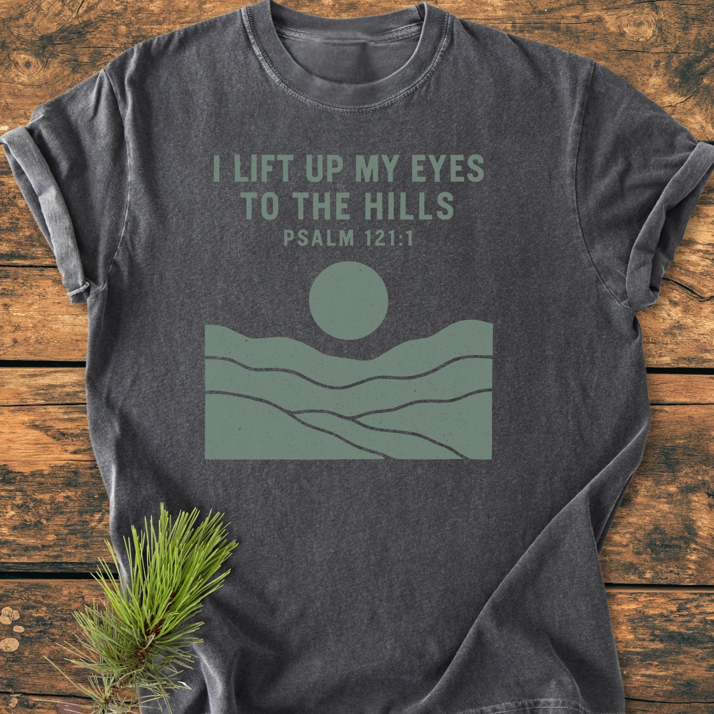 I Lift Up My Eyes - Vintage Wash Tee: Charcoal-gray T-shirt with Psalm 121:1 in muted green and a graphic of hills and sun; rustic look enhanced by a pine sprig beside it.
