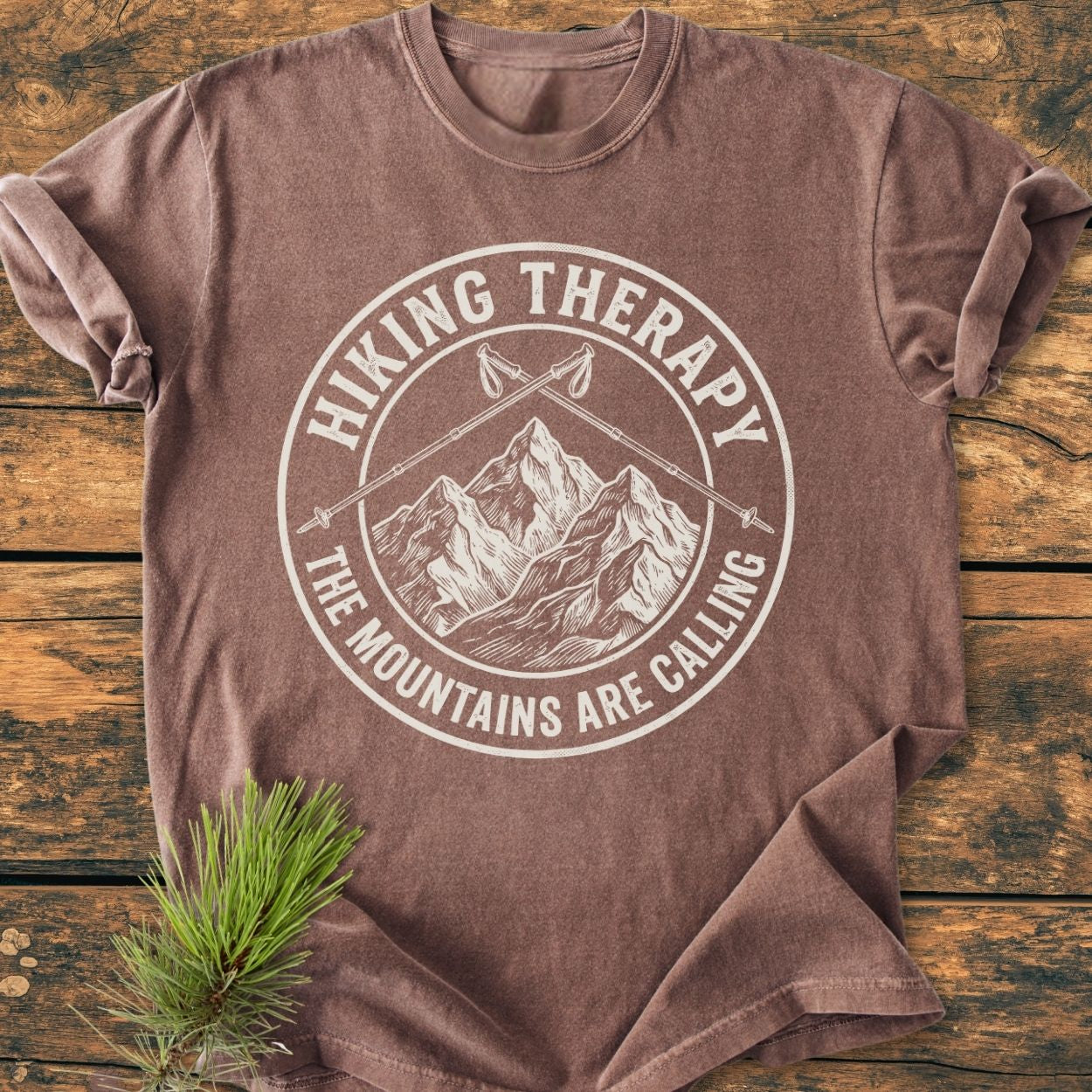 Hiking Therapy - Vintage Wash Tee features a circular mountain graphic with hiking poles, laid on wood; soft, relaxed fit, 100% ring-spun cotton, embodying comfort and durability.
