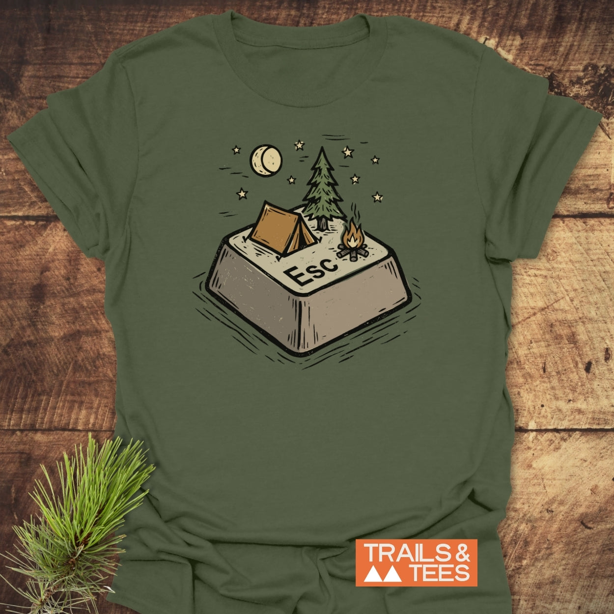 Escape T-Shirt featuring a campsite graphic on an oversized Esc key, with a tent, pine tree, campfire, crescent moon, and stars. Logo TRAILS & TEES. on the bottom corner.