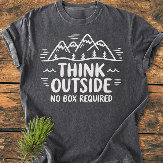 Think Outside - Vintage Wash Tee features a mountain-and-tree design with the slogan “THINK OUTSIDE NO BOX REQUIRED” on charcoal-gray fabric, complemented by a pine sprig, showcasing its outdoor-inspired theme.