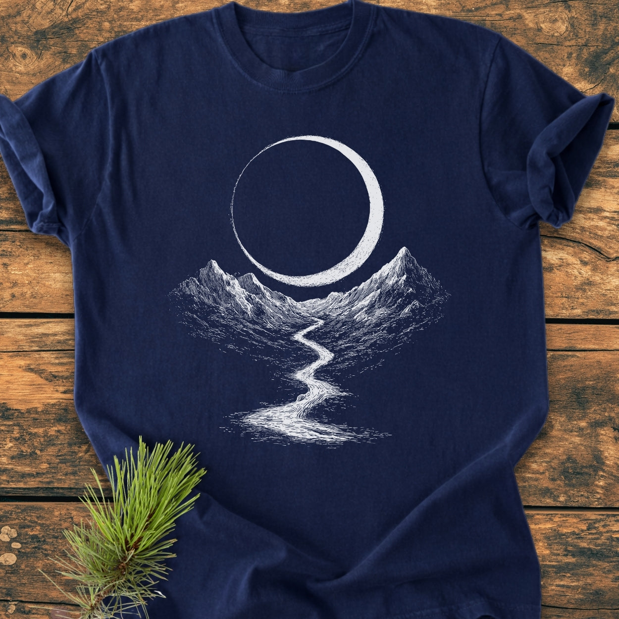 Eclipse Trail - Vintage Wash Tee features a dark-navy design with a crescent moon, mountains, and river. A sprig of pine accents the soft, ring-spun cotton shirt, showcasing its relaxed fit.