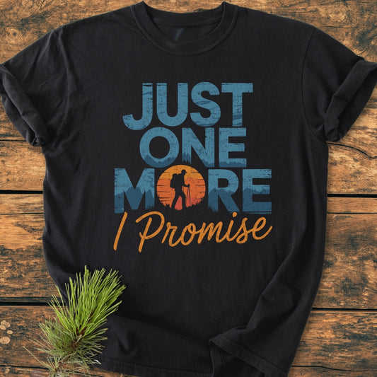 Just One More I Promise - Vintage Wash Tee: Black T-shirt with “JUST ONE MORE” and hiker silhouette design. Laid on wood, featuring a relaxed fit and soft-washed, garment-dyed fabric for comfort.