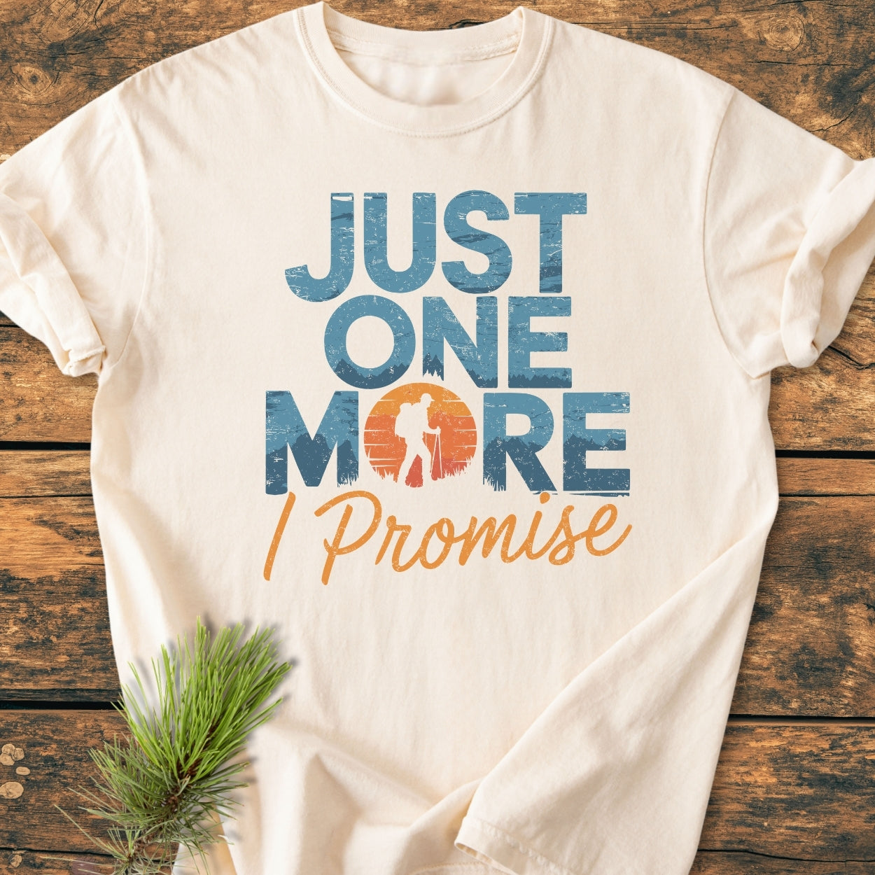Just One More I Promise - Vintage Wash Tee featuring a hiker silhouette in the O of MORE, laid on wood with pine sprig, highlighting its cozy, relaxed fit and durable design.