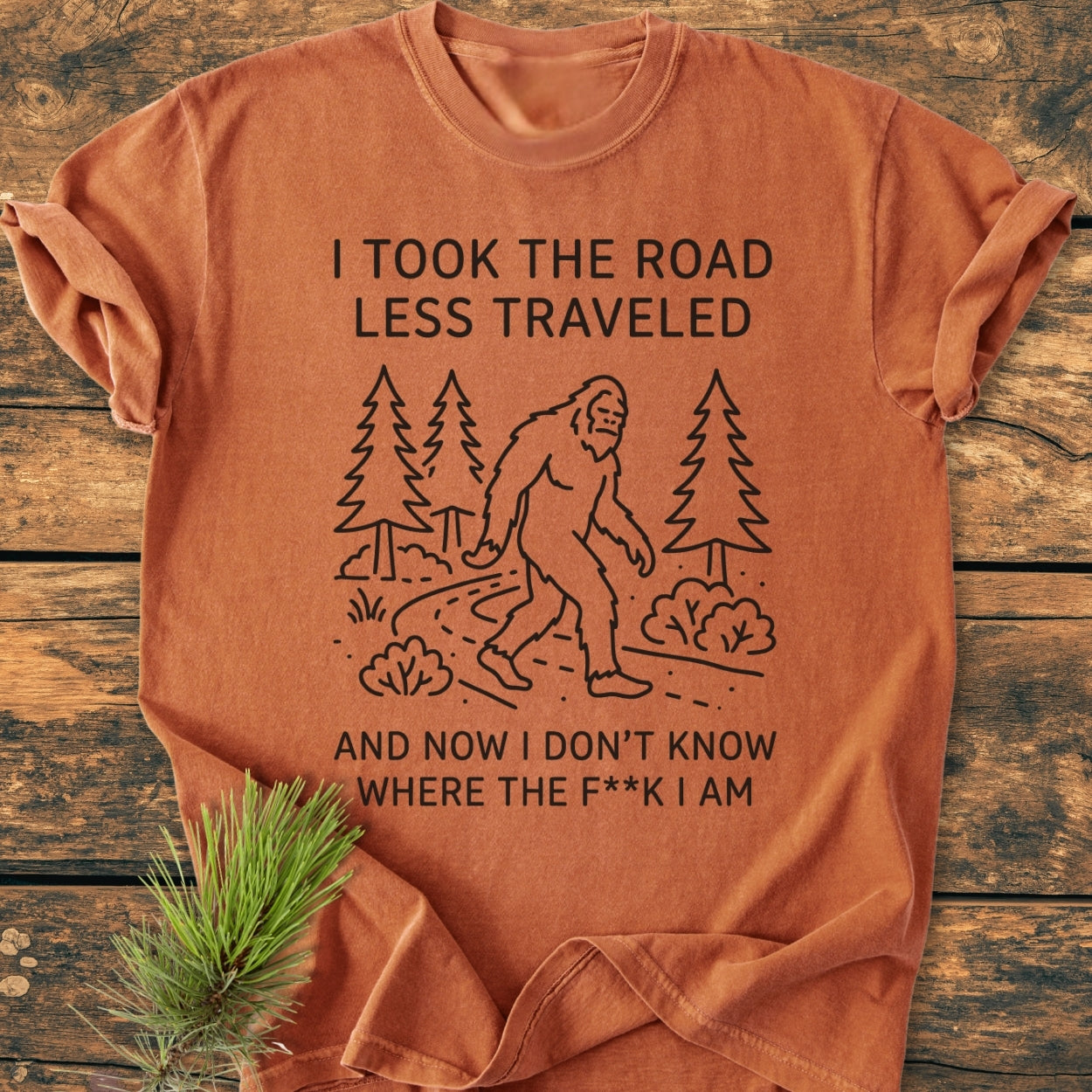 I Took The Road Less Traveled - Vintage Wash Tee features Bigfoot on a trail, printed on a rust-colored shirt, offering a relaxed fit and soft-washed, durable, 100% ring-spun cotton.