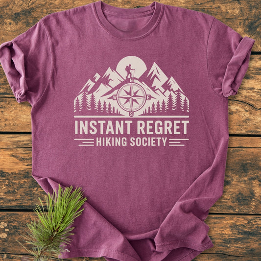 Instant Regret Hiking Society - Vintage Wash Tee features a stylized mountain and forest design with a lone hiker. The heathered purple tee, made of soft, durable cotton, promises comfort and style.