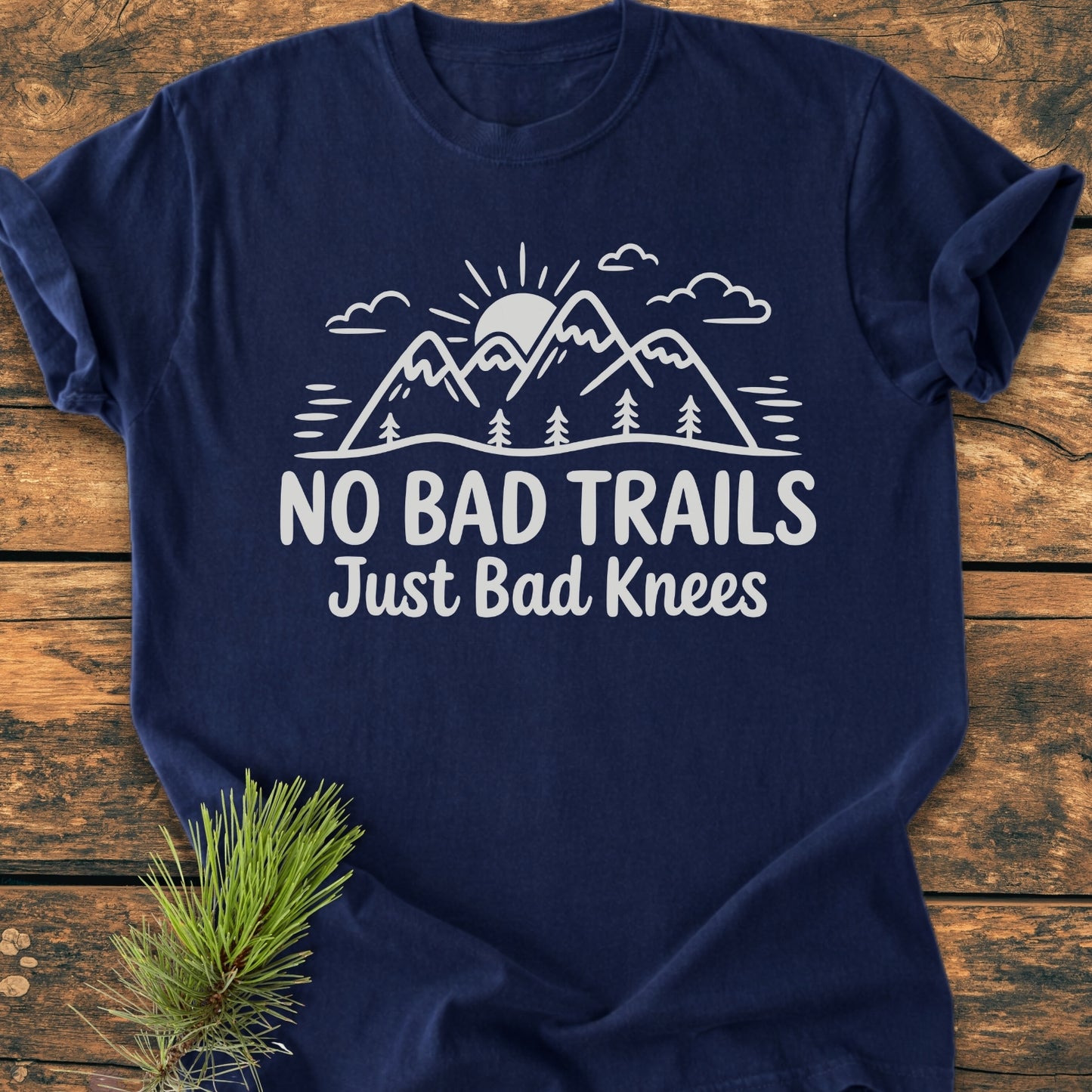 No Bad Trails - Vintage Wash Tee features a mountain and sun graphic with the slogan NO BAD TRAILS Just Bad Knees, displayed on a navy-blue Comfort Colors garment-dyed T-shirt laid flat.