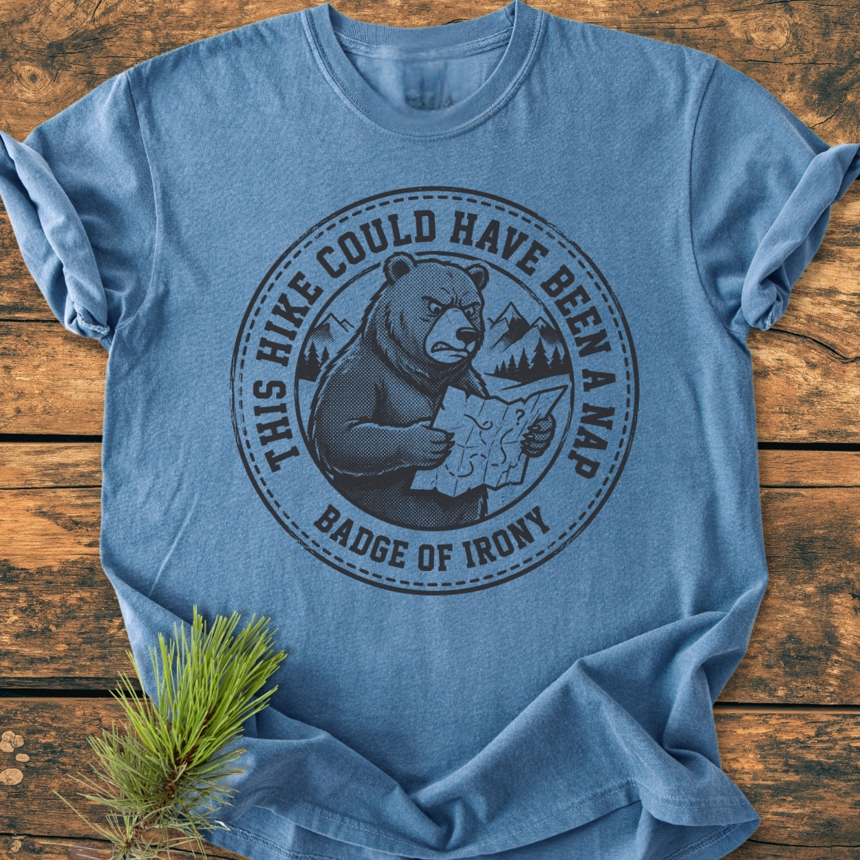 Heather-blue Could Have Been A Nap - Vintage Wash Tee featuring a disgruntled bear illustration with a map, highlighting irony. Laid on wood with pine sprig, showcasing soft, durable, ring-spun cotton fabric.