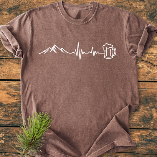 Mountains And Beer - Vintage Wash Tee with a stylized mountain, heartbeat line, and beer mug graphic, laid flat with a pine sprig accent. Crafted from soft, durable, ring-spun cotton for relaxed comfort.