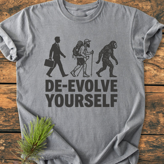 De-Evolve Yourself - Vintage Wash Tee features black silhouettes of a businessman, hiker, and ape with DE-EVOLVE YOURSELF. slogan on a grey, soft-washed, relaxed-fit t-shirt.