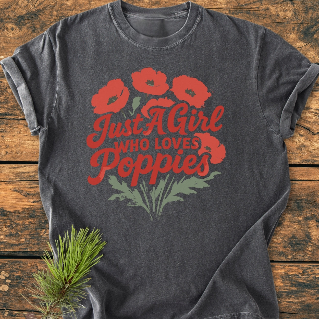 Just A Girl Who Loves Poppies - Vintage Wash Tee: Charcoal T-shirt featuring vibrant red poppies and bold red script, laid on wooden surface with pine sprigs, showcasing a cozy, relaxed-fit design.