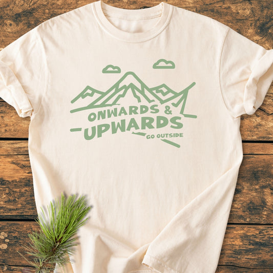Go Outside - Vintage Wash Tee featuring a mountain range and ONWARDS & UPWARDS design in sage green, laid flat on wood with pine sprig, showcasing its relaxed fit and soft, garment-dyed texture.