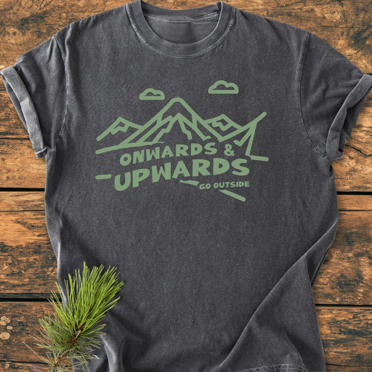 Go Outside - Vintage Wash Tee featuring a mountain line-drawing and slogan, laid on wood with a pine bough accent. Made from soft, garment-dyed, ring-spun cotton for comfort and durability.