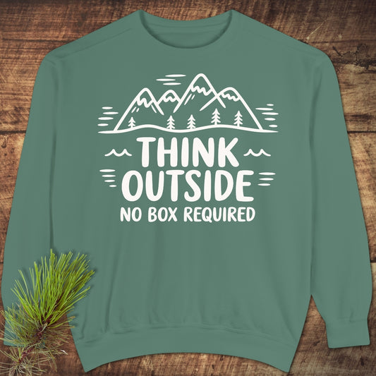 Think Outside Sweatshirt in teal-green, featuring a white line-drawing of mountains and trees with the slogan THINK OUTSIDE NO BOX REQUIRED, laid flat on a wooden background with a pine sprig accent.
