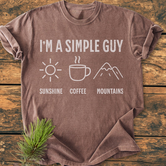 I'm A Simple Guy - Sunshine Coffee Mountains - Vintage Wash Tee: Brown, short-sleeve T-shirt with white text and icons, laid on wood, pine sprig beside. Comfortable, relaxed fit, 100% ring-spun cotton.