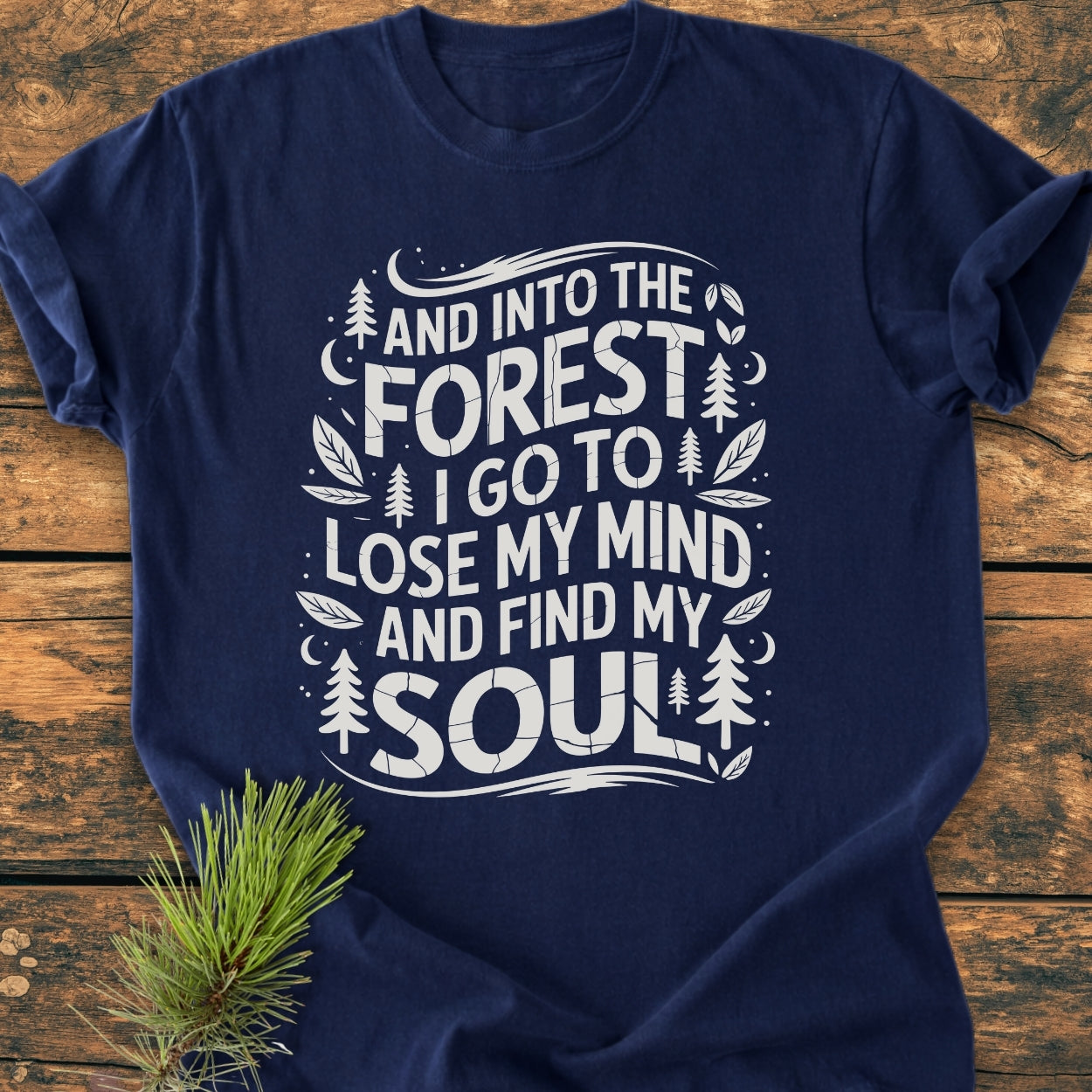 Navy-blue And Into The Forest I Go - Vintage Wash Tee featuring white woodland-themed typography and graphics, laid flat with a pine sprig accent, showcasing its relaxed, durable design.