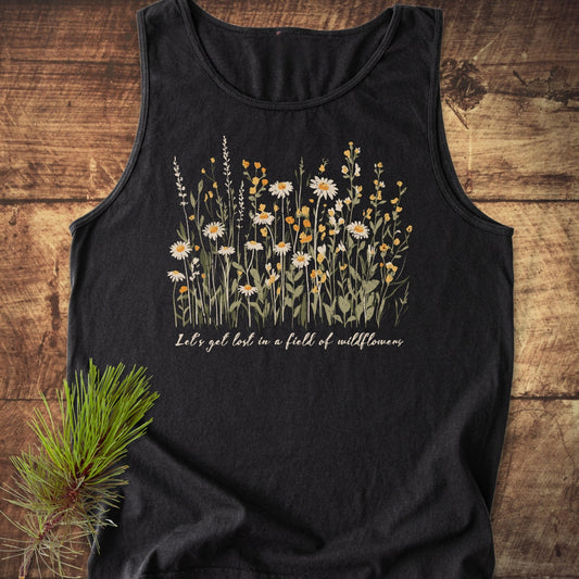 Let's Get Lost In A Field Of Wildflowers Tank Top on rustic wood, featuring white and yellow floral illustration with hand-lettered text, enhanced by a natural pine sprig for an outdoorsy vibe.