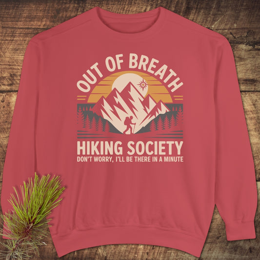 Out Of Breath Hiking Society Sweatshirt features a mountain graphic with a hiker, sun, and pine trees. Laid flat, this casual unisex sweatshirt exudes comfort with a relaxed fit and detailed design.