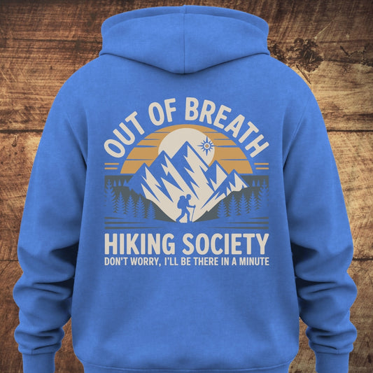 Out Of Breath Hiking Society BACKPRINT on a royal-blue hoodie featuring a sun setting behind mountains with a hiking silhouette and pine trees, complemented by hiking-themed slogans.