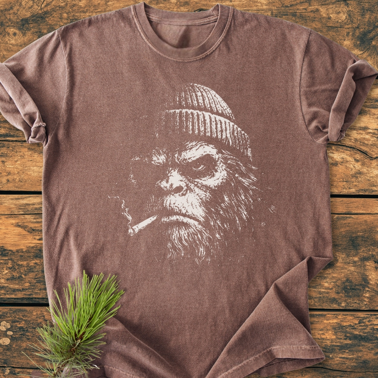 Slow Burn Club - Vintage Wash Tee featuring a bearded figure sketch with a cigarette, on a brown crew-neck laid flat, complemented by a pine sprig, showcasing its relaxed fit and durable stitching.