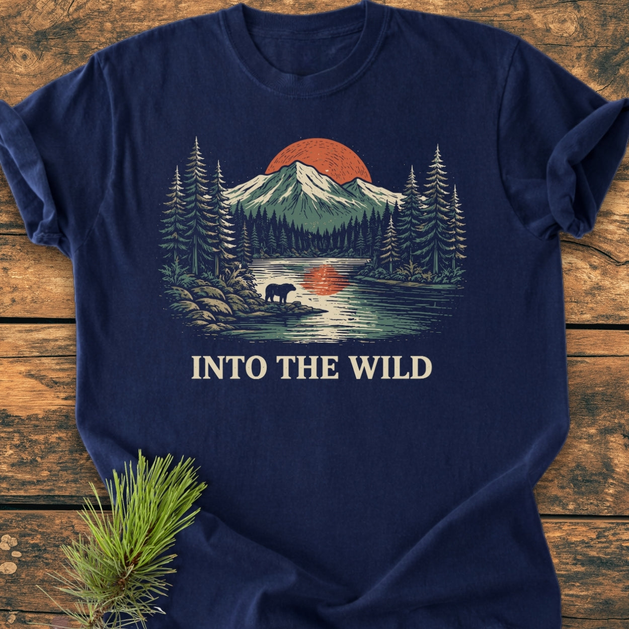 Into The Wild - Vintage Wash Tee displays a wilderness scene with pine trees, mountains, a red sun, and a bear silhouette, on a navy-blue Comfort Colors garment-dyed T-shirt.