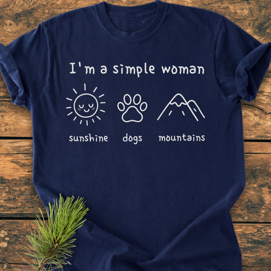 I'm A Simple Woman - Sunshine, Dogs, Mountains - Vintage Wash Tee displayed on wood, features a navy-blue color, relaxed fit, and white icons with corresponding labels on the chest.