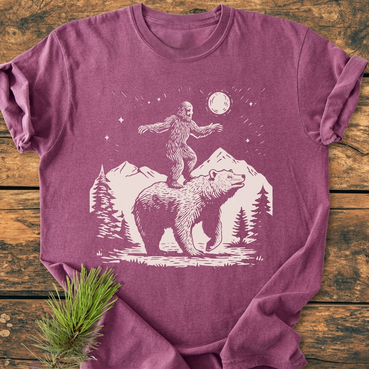 Bigfoot And Bear - Vintage Wash Tee features a heather-purple color with an outdoor-themed illustration of Bigfoot and a bear, set against pine trees, mountains, and a celestial sky.