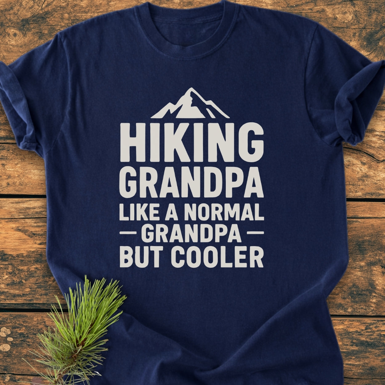 Hiking Grandpa - Vintage Wash Tee features a white mountain silhouette and bold text, HIKING GRANDPA LIKE A NORMAL GRANDPA—BUT COOLER, on a navy-blue T-shirt, laid on rustic wood.