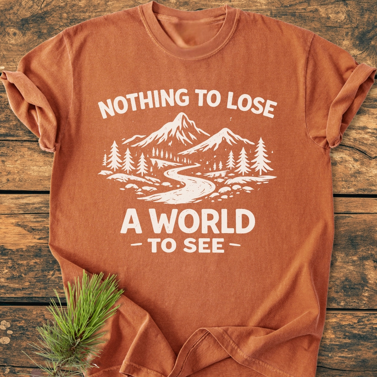 Nothing To Lose - Vintage Wash Tee featuring a mountains and trees design with slogan, laid flat with a pine sprig, showcasing its soft, relaxed fit, garment-dyed, ring-spun cotton construction.
