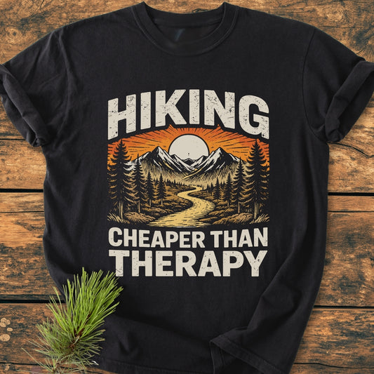 Hiking Cheaper Than Therapy - Vintage Wash Tee features a scenic outdoor print with mountains and forest. Laid on wood, it highlights a cozy, relaxed fit, ideal for everyday wear.