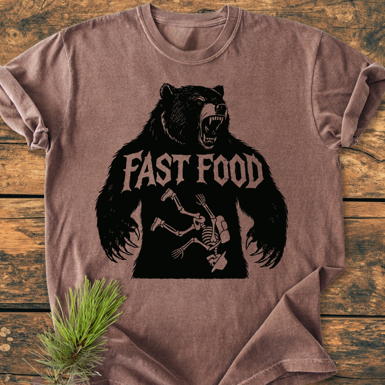 Fast Food - Vintage Wash Tee features a washed-out brown color with a roaring bear silhouette and human skeleton graphic, laid flat on wood. Includes FAST FOOD text above the design.