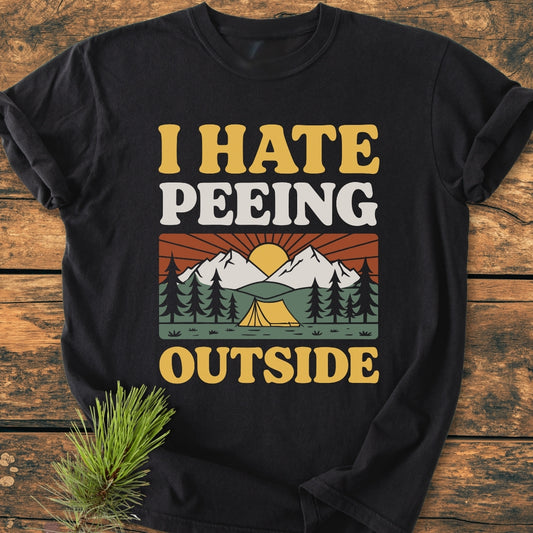 Black T-shirt with retro camping graphic featuring pine trees, tent, mountains, and sun. Vintage font reads “I HATE PEEING OUTSIDE.” Relaxed fit, 100% ring-spun cotton, durable, tubular shape.