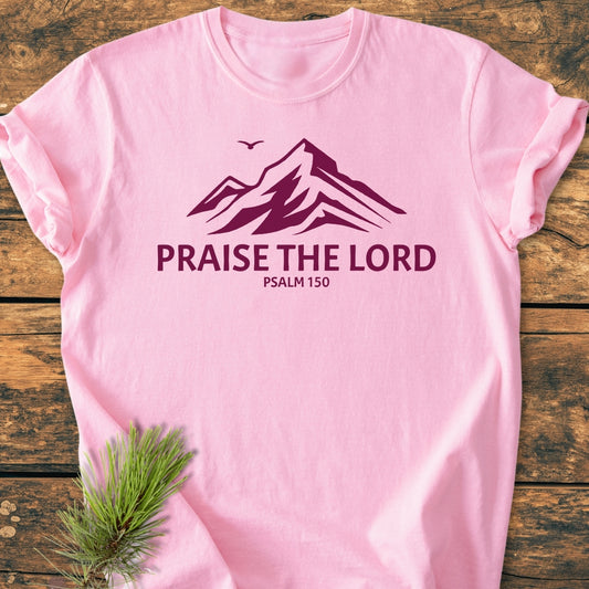 Praise The Lord, Psalm 150 - Vintage Wash Tee features a mountain graphic and bird silhouette in dark purple, with PRAISE THE LORD and PSALM 150 text, laid flat with pine sprig accent.