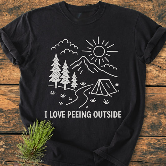 I Love Peeing Outside - Vintage Wash Tee featuring a white line-drawing of nature scene with slogan on a black T-shirt, laid on wooden surface, showcasing a cozy, relaxed fit and durable stitching.
