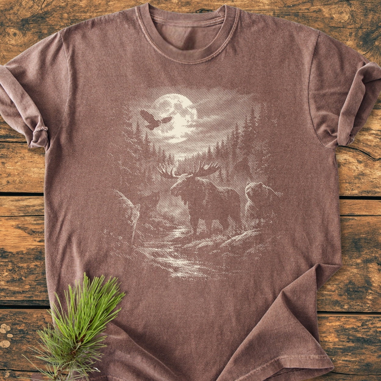 Moonlit Woodland - Vintage Wash Tee featuring a moonlit forest scene with an owl, moose, and wildlife, laid flat on wood. Crafted from soft, durable, pre-shrunk 100% ring-spun cotton.