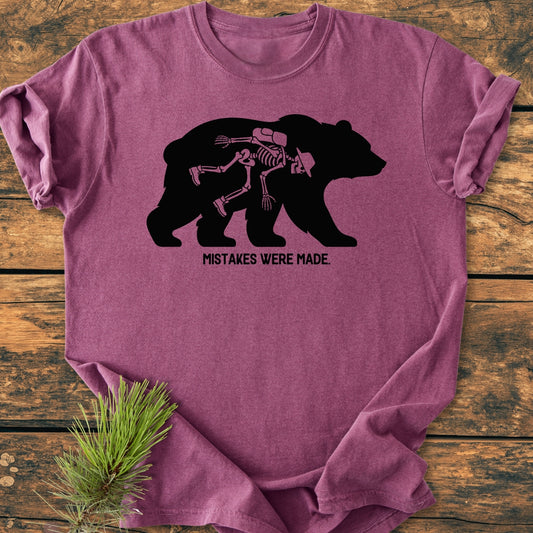 Mistakes Were Made - Vintage Wash Tee features a bear with a skeleton graphic on a heathered plum-purple background, laid flat on wood with a pine sprig, emphasizing comfort and relaxed fit.