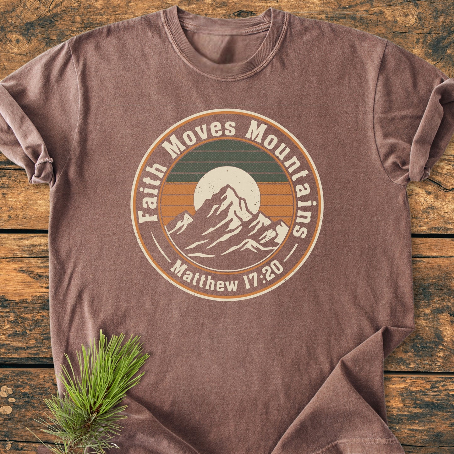 Faith Moves Mountains - Vintage Wash Tee featuring a mountain range graphic with a sun and stripes, text from Matthew 17:20, on a soft heather-brown cotton shirt with rustic pine branch accent.