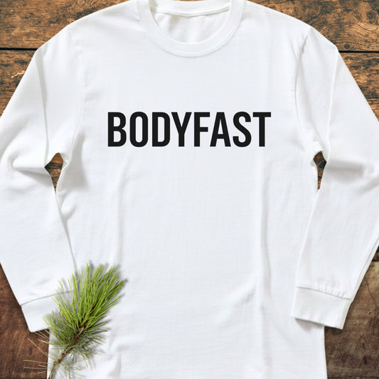BODYFAST Long-Sleeve Tee in white, featuring bold black lettering across the chest. Laid flat with a pine sprig accent, showcasing its relaxed fit and soft, garment-dyed 100% ring-spun cotton fabric.
