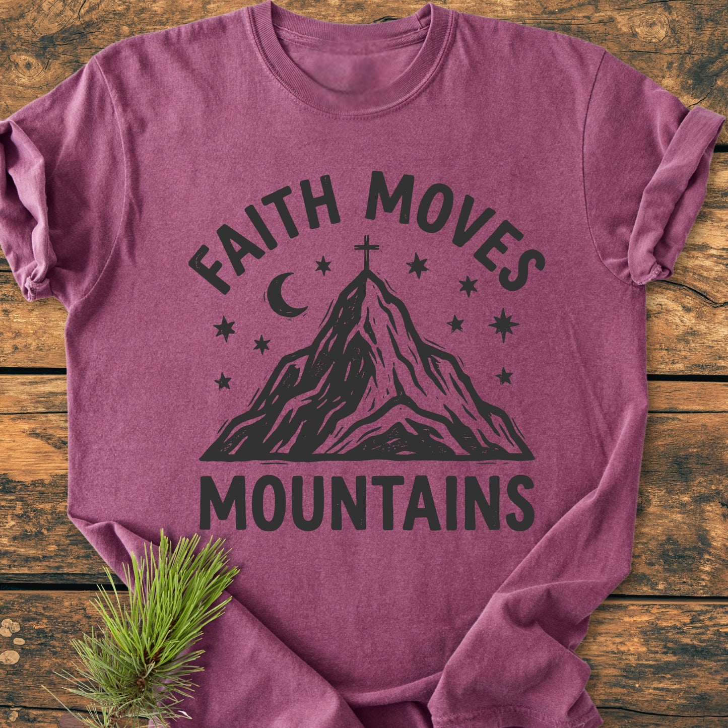 Faith Moves Mountains - Vintage Wash Tee featuring a faith-inspired graphic with “FAITH MOVES MOUNTAINS,” a mountain peak, cross, stars, and moon, displayed on a rustic wooden surface with pine.