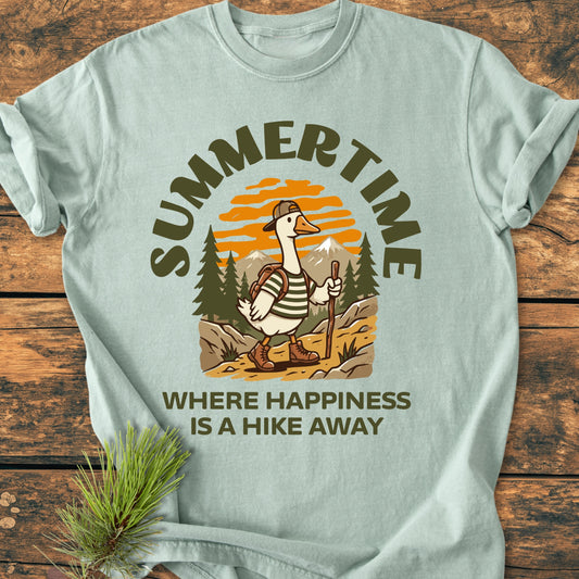 Summertime Hike - Vintage Wash Tee featuring a hiking cartoon goose under an orange sunset, laid on a wooden surface with a pine sprig, highlighting its cozy, relaxed fit and durability.