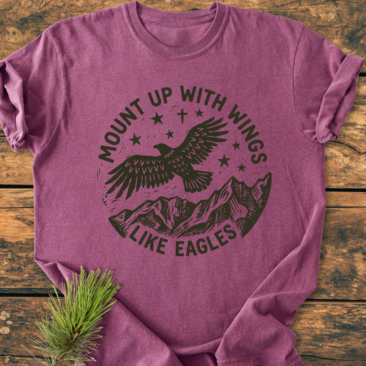 Mount Up With Wings - Vintage Wash Tee features a heather-purple hue with a stamp-style graphic of an eagle and mountains. Laid on wood, it includes a pine sprig detail for added rustic charm.