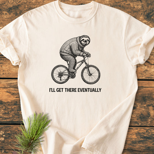 I'll Get There Eventually - Vintage Wash Tee featuring a sloth on a bicycle graphic, laid on wood with pine sprigs, showcasing soft-washed, ring-spun cotton for a cozy, relaxed fit.