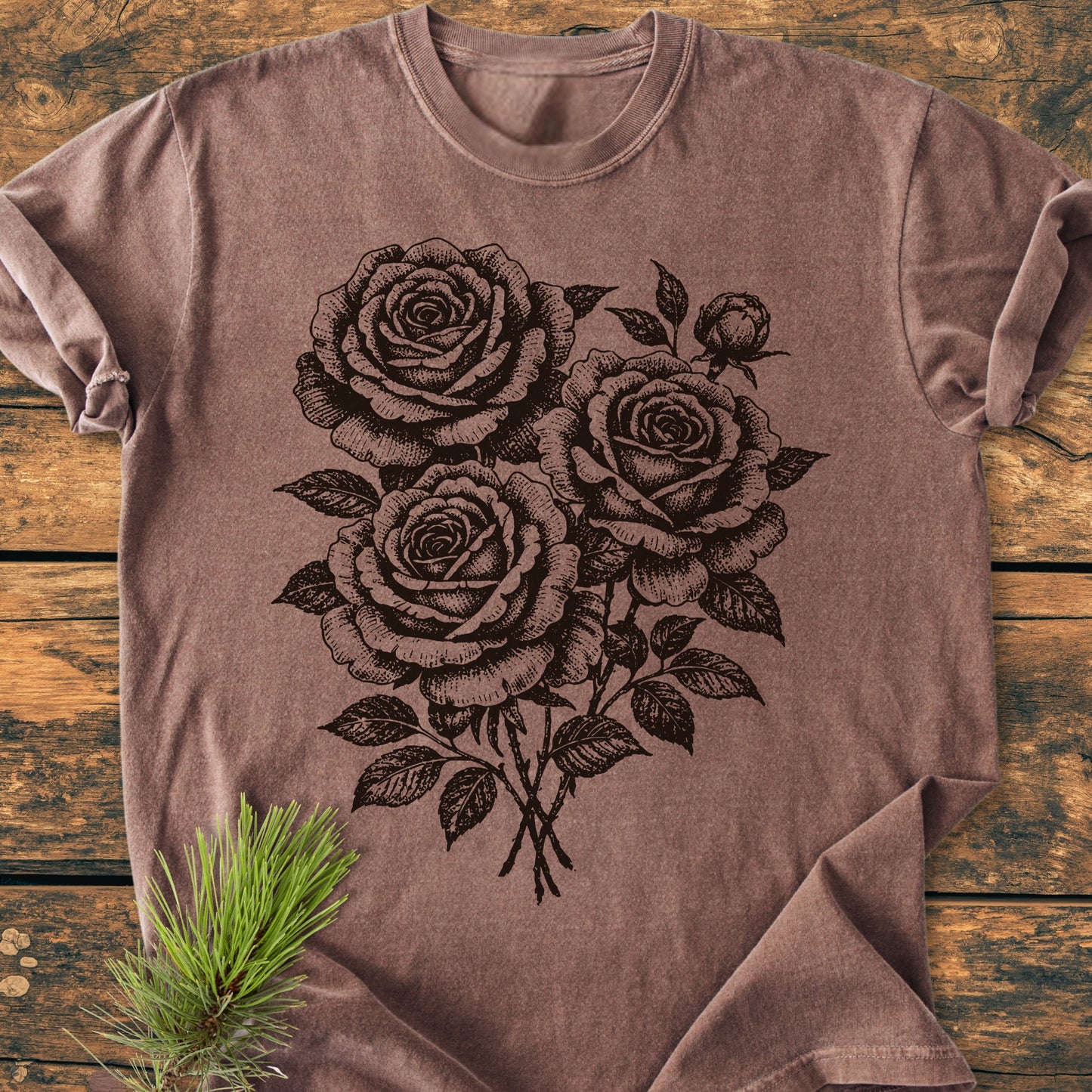 Rose Bouquet - Vintage Heavyweight Tee, soft brown crew-neck, features a black line-drawing of three roses and a bud. Laid on rustic wood, a green pine sprig accents this customizable, ring-spun cotton tee.