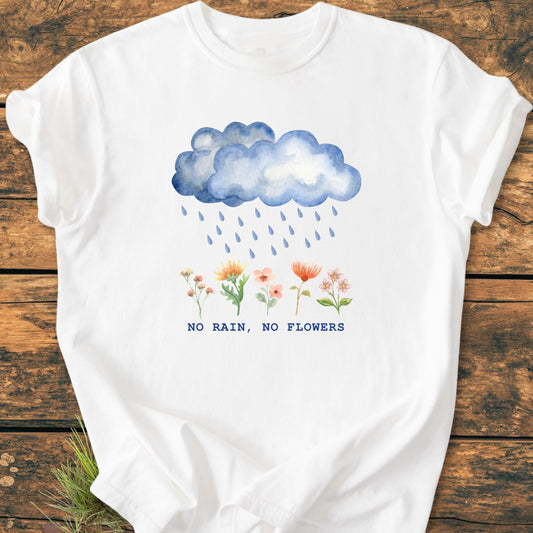 No Rain No Flowers - Vintage Heavyweight Tee features a watercolor-style blue rain cloud illustration above wildflowers with the slogan “NO RAIN, NO FLOWERS,” laid flat on a wooden surface.