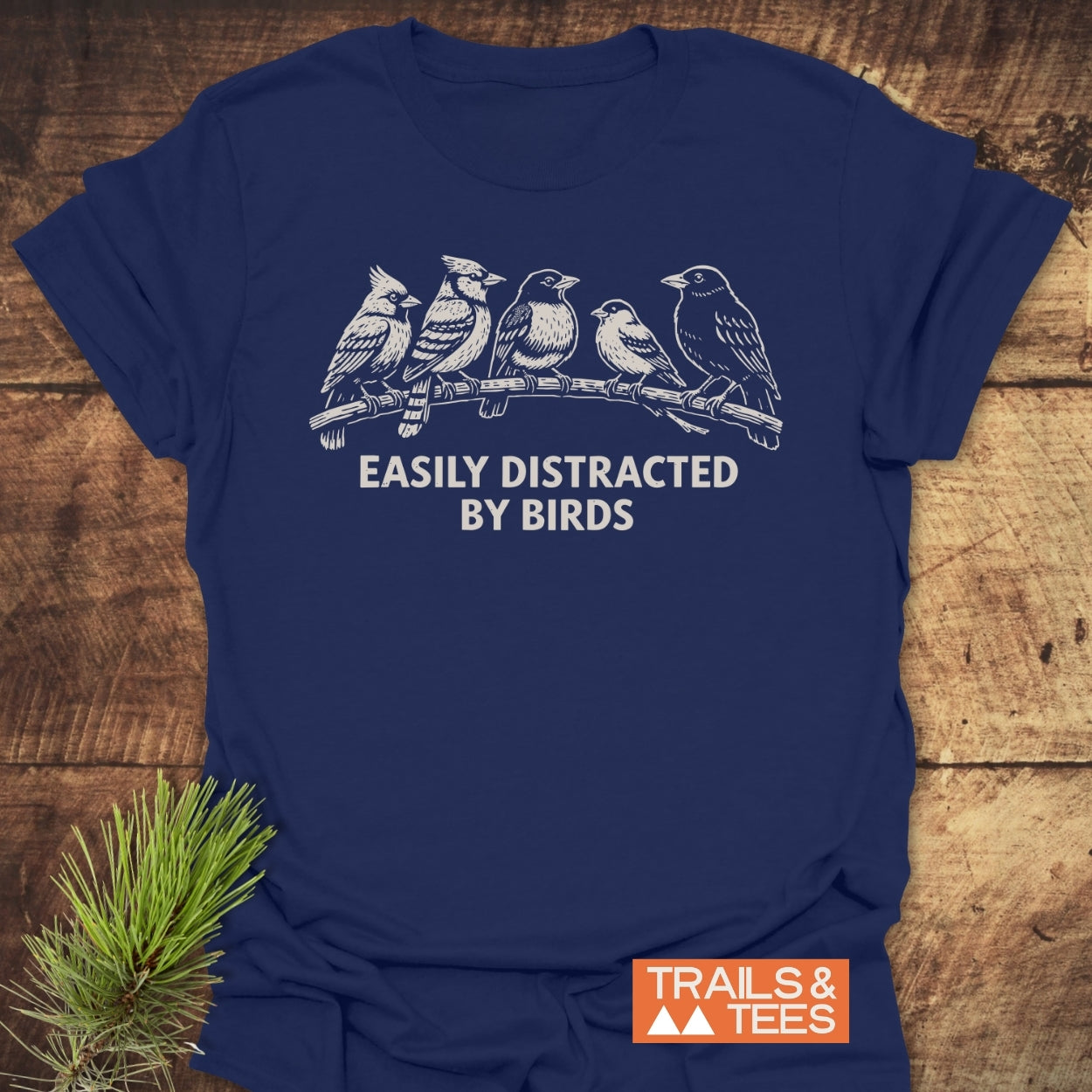 Easily Distracted By Birds T-Shirt featuring a white line-drawing of songbirds and phrase, on navy-blue cotton. Includes small TRAILS & TEES logo, highlighting outdoor adventure spirit.