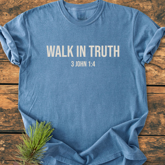 Heather-blue Walk In Truth - Vintage Wash Tee laid flat, featuring bold lettering with a biblical reference. A pine sprig accents the scene, emphasizing the tee's rustic, relaxed appeal.