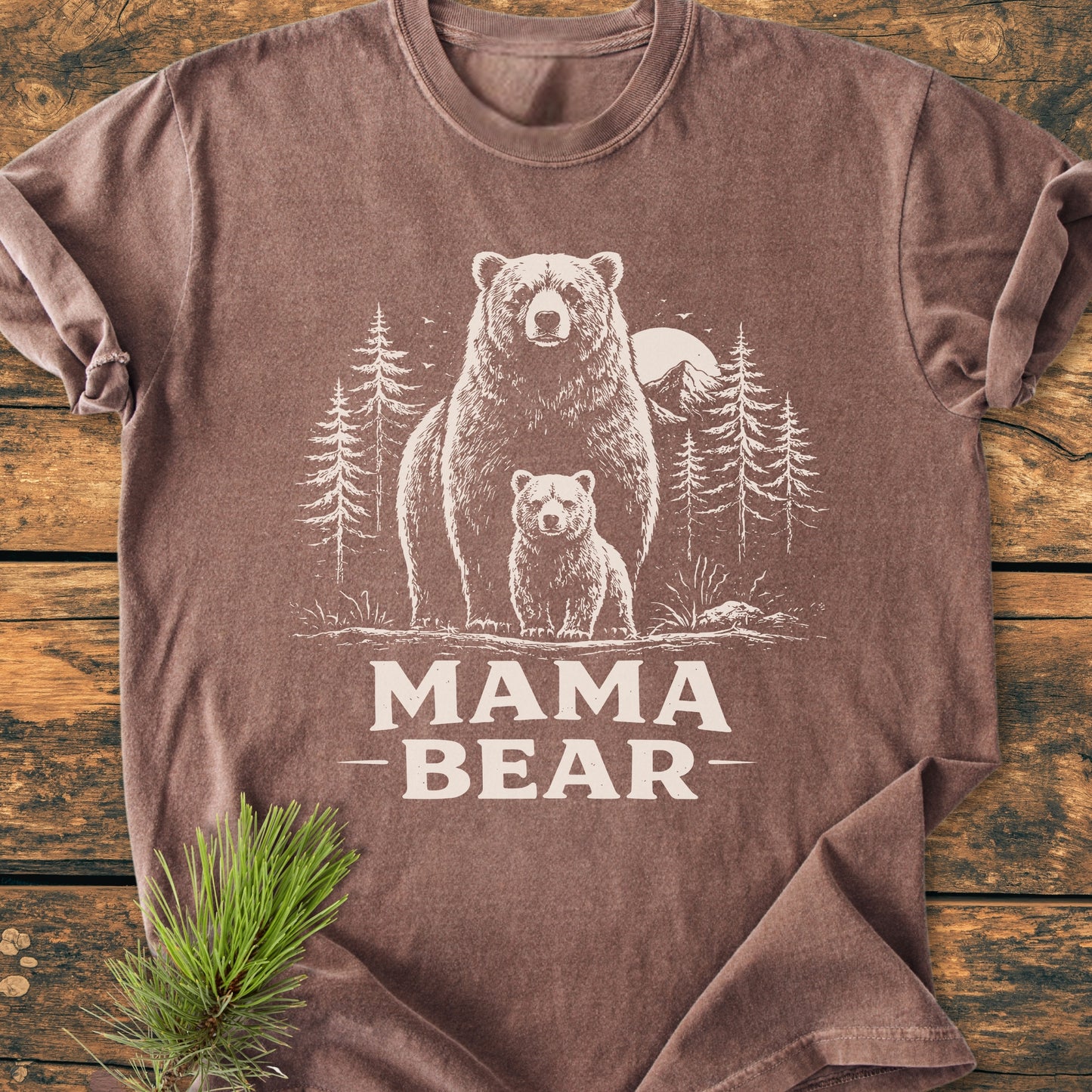 Mama Bear - Vintage Heavyweight Tee: Brown short-sleeve shirt with MAMA BEAR printed beneath a bear and cub illustration, framed by pine trees, moon, and mountains, showcasing rustic charm and durability.