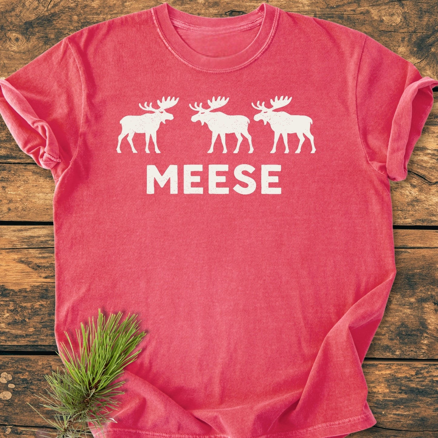 Red Meese Vintage Wash Tee with three white moose silhouettes, laid on wood. Ideal for moose enthusiasts and pun lovers, offering a relaxed fit and vintage feel.
