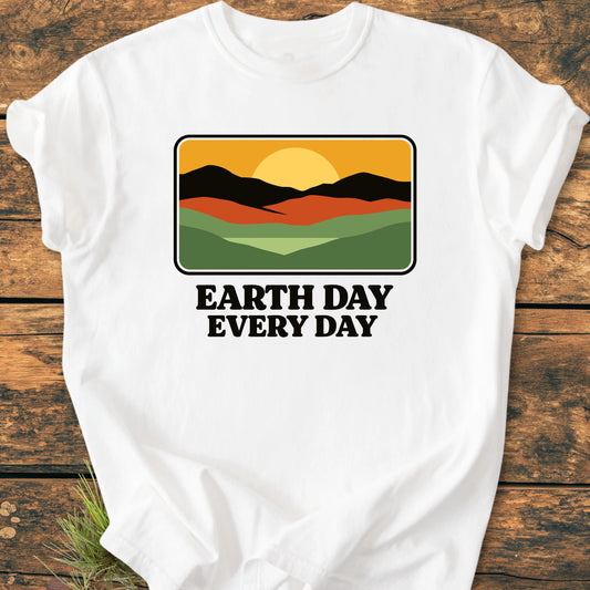White T-shirt featuring a retro-style graphic of hills and sun with EARTH DAY EVERY DAY text, laid on wood. Vintage wash for a soft, relaxed unisex fit.